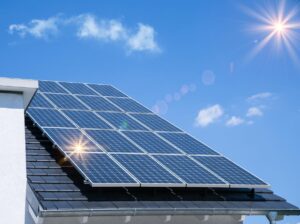 青空と太陽が背景。太陽光パネルが設置された屋根のみの画像